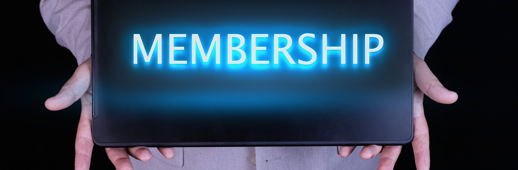 MEMBERSHIP word, text written in neon letters on a laptop which is being held by a businessman in a gray suit.
